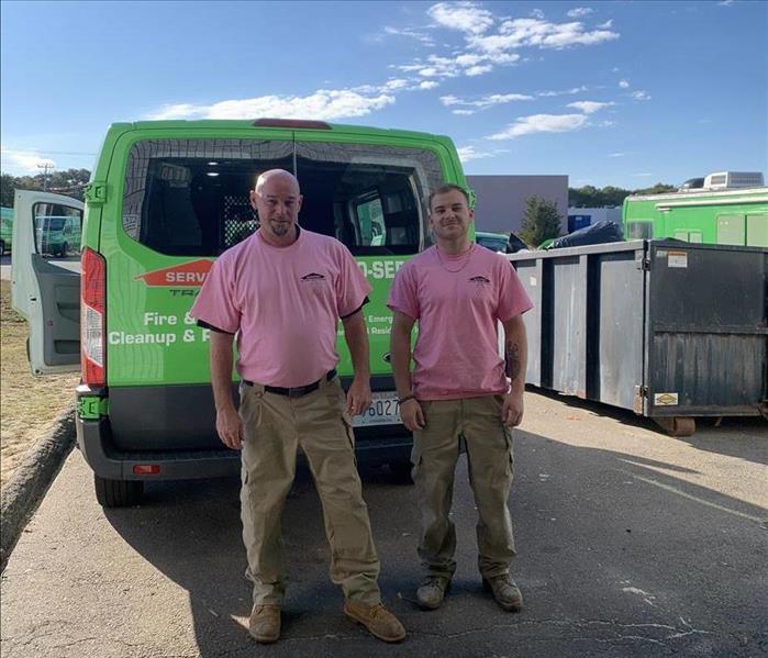 two employees in pink cancer shirts in front of servpro vehicle